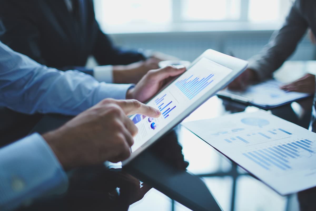 Profissional analisando gráficos em tablet durante reunião, representando um guia básico de investimento em equipe.