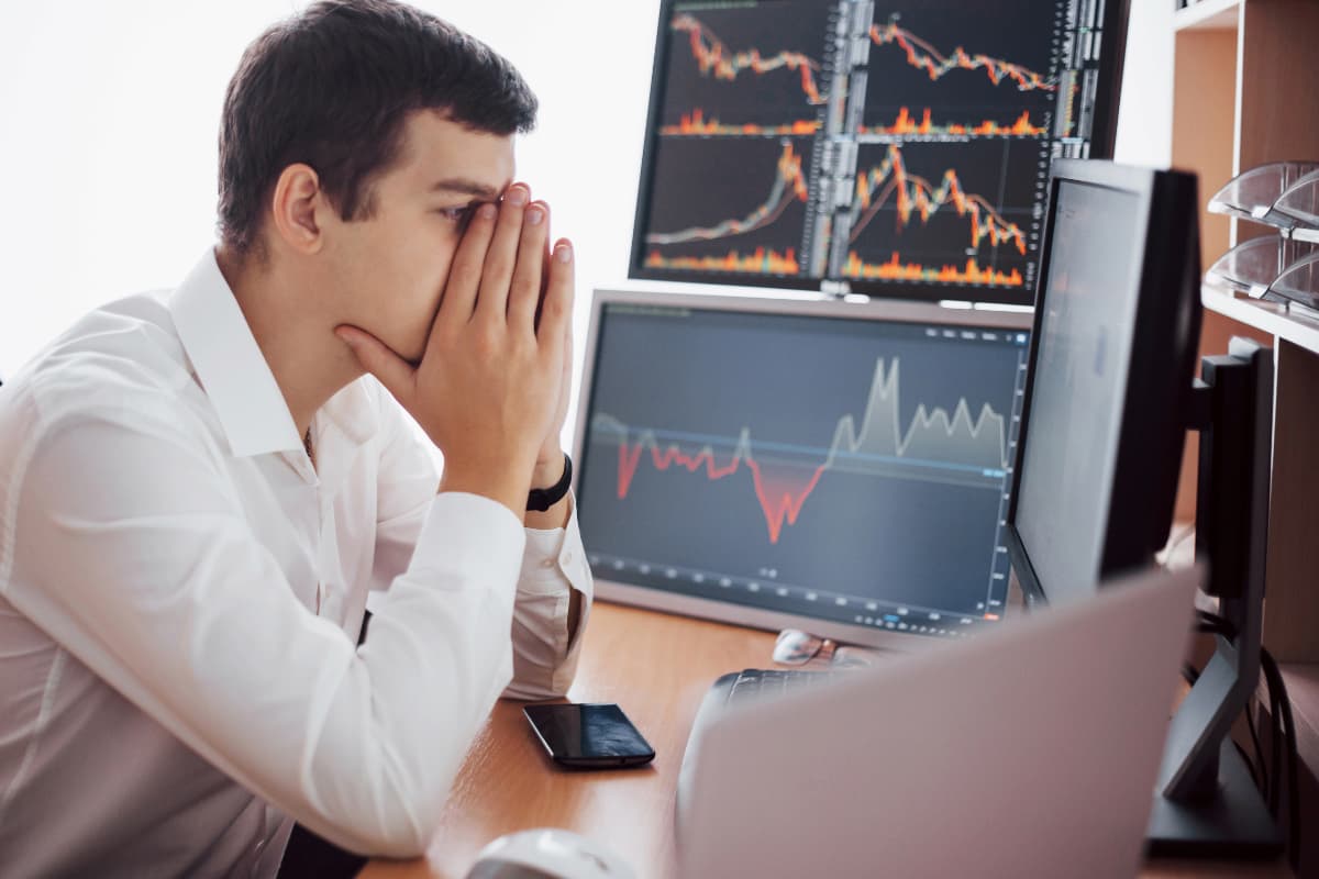 Homem preocupado observa gráficos financeiros em queda, ilustrando erros comuns sobre investimentos alternativos.