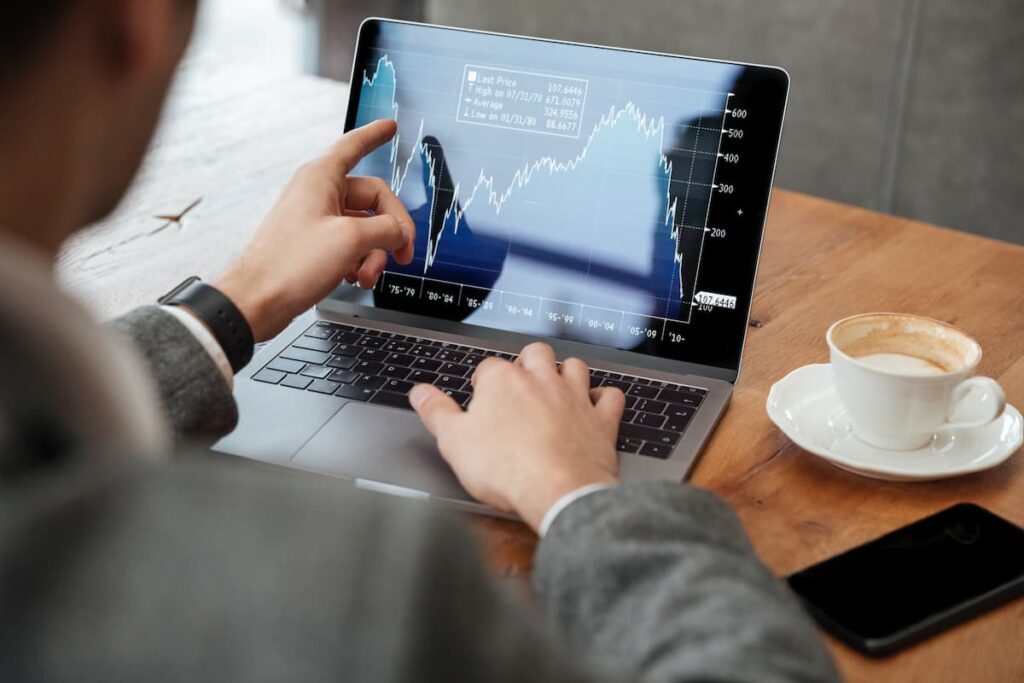 Pessoa analisando gráfico financeiro em notebook com café ao lado, ilustrando um guia básico de investimento para iniciantes.