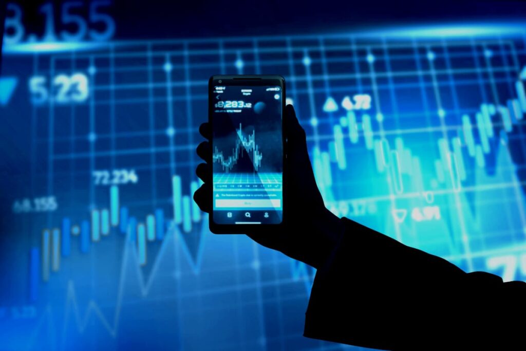 Pessoa segura celular com gráficos financeiros, representando análise de investimentos alternativos no mercado digital.