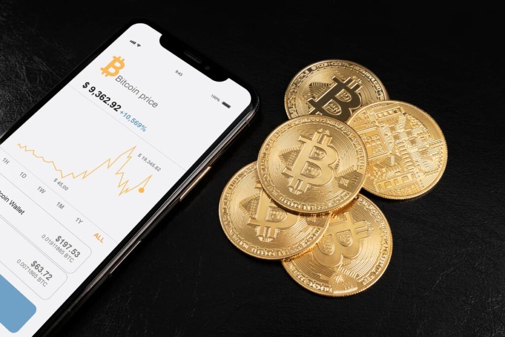 Celular com gráfico de Bitcoin e moedas douradas ilustrando dúvida comum: qual o valor mínimo para investir em criptomoedas.