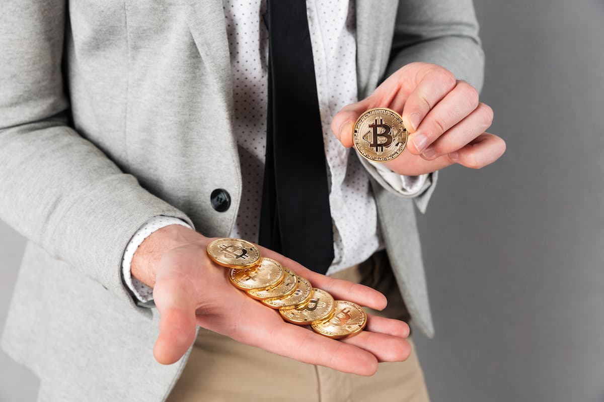 Homem de terno segurando bitcoins, representando a dúvida: qual o valor mínimo para investir em criptomoedas.