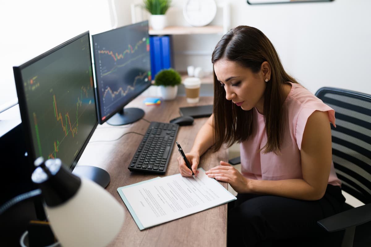 Mulher analisando gráficos e preenchendo documento, representando conceitos do glossário de investimentos.