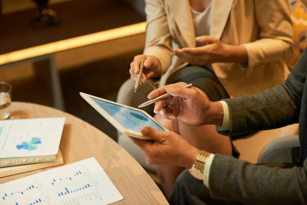 Executivos analisando gráficos em tablet e papéis durante reunião sobre investimentos alternativos no Brasil.