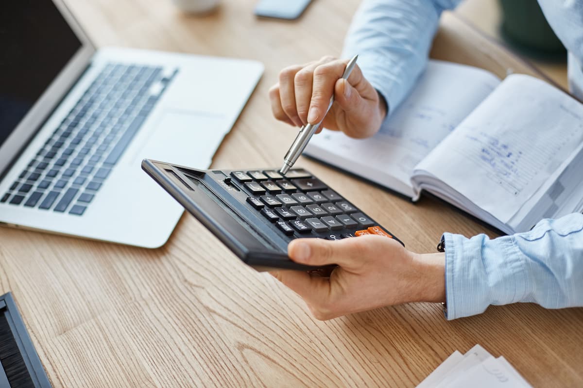 Pessoa usando calculadora e analisando anotações ao lado de notebook, ilustrando a tributação de investimentos no exterior.