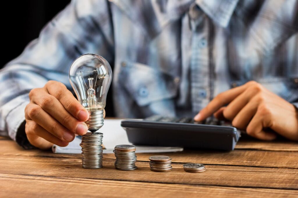 Homem segurando uma lâmpada sobre pilhas de moedas, simbolizando ideias e retorno em investimentos alternativos no Brasil.
