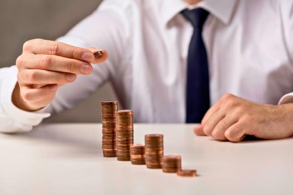 Homem empilha moedas em ordem crescente, simbolizando estratégias sobre onde investir no 2º semestre de 2025.