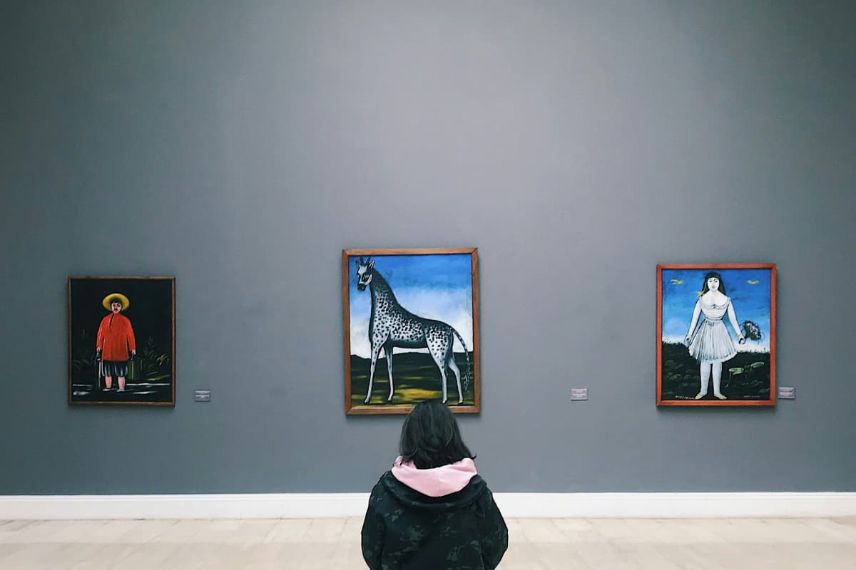 Pessoa observa obras coloridas em museu, refletindo por que investir em arte pode ser uma forma de valorizar o patrimônio.
