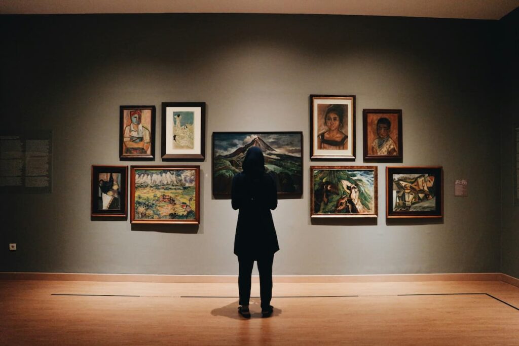 Pessoa observando quadros em galeria de arte, refletindo sobre por que investir em arte pode ser uma escolha valiosa.