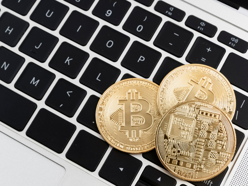 A imagem é uma fotografia minimalista e em ângulo superior que foca em moedas de criptomoeda sobre um laptop.