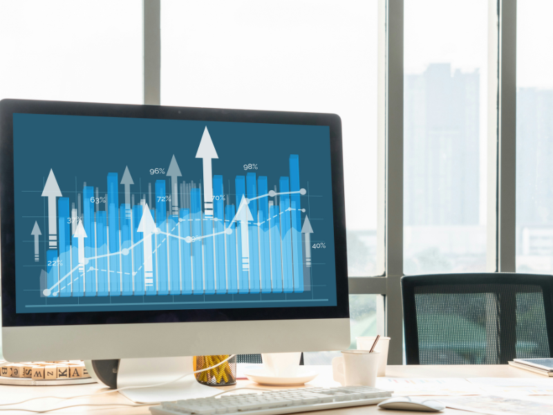 A imagem mostra a tela de um monitor de computador com um gráfico em tons de azul. O gráfico, que tem barras e setas apontando para cima, indica crescimento e progresso.