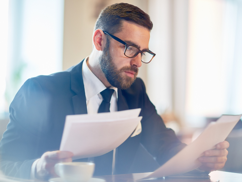 Homem de negócios com expressão séria analisando documentos financeiros em um ambiente profissional, simbolizando análise de investimentos e tomada de decisões estratégicas.