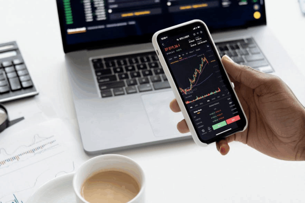 A imagem ilustra uma cena de negociação financeira, investimento ou análise de mercado, com foco na portabilidade e no uso de tecnologia para acompanhar ativos. O título do arquivo ("Ativos para Multiplicar Patrimônio.jpg") confirma o contexto de finanças e investimentos.