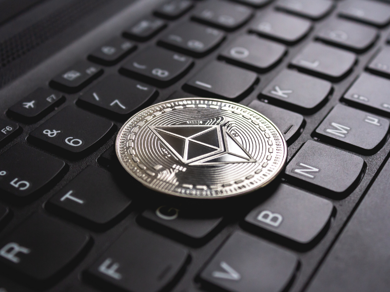 A imagem mostra uma moeda física metálica com o símbolo do Ethereum posicionada sobre o teclado de um notebook.